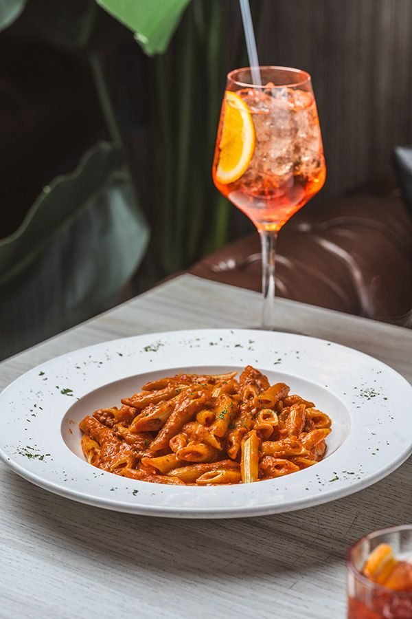Penne en salsa roja junto a un Aperol Spritz